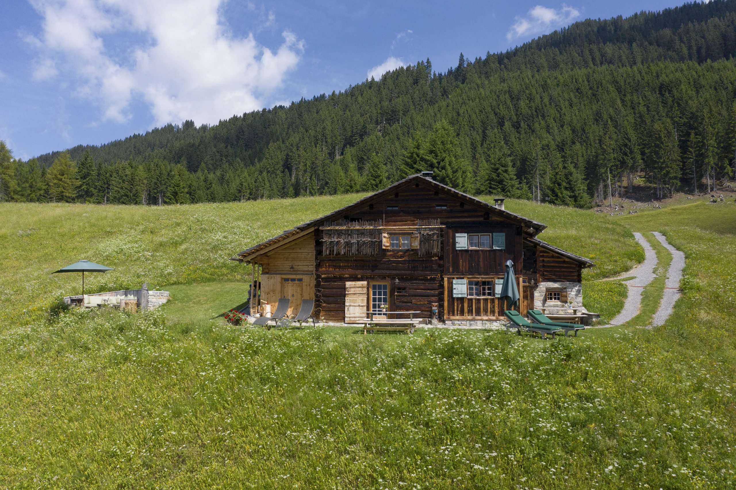 ferienhaus auf einer großen wiese am berg mit liegen und sonnenschirm